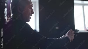 Medium shot of sportsman in compression garments leaning on punching bag and wrapping his hands with elastic bandage to protect them against injuries
