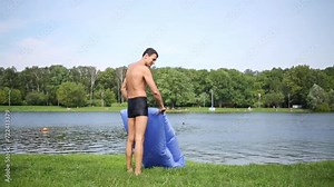 Man in swim briefs torque, close air inflatable sofa and lie on it