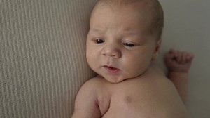 Newborn baby boy lying in bed and lloking around seriously. Infant child portrait at home