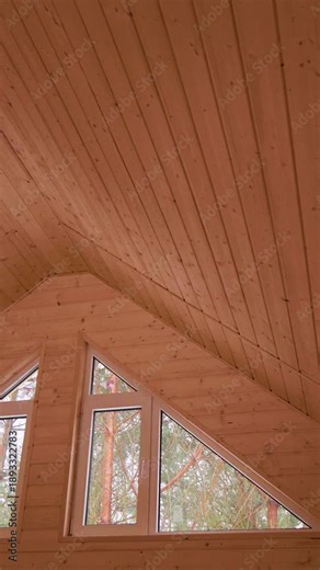 A wooden ceiling triangular windows reveals a view of trees outside. Ideal for architectural design showcases, interior decor inspiration, and construction projects. Smooth panning camera movement