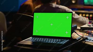 Sound designer and singer look at laptop with isolated display in control room, operating mixing console and volume level buttons to create a hit song. Artist working with audio expert. Camera A.