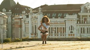 A young woman with long legs in small shorts performing attractive dancing on the roof - go down and spreading her legs- bright sunset