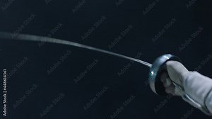 Professional fencer in protective uniform practicing maneuvers with sword alone in dark studio . Fencing demonstration on black smoked background . Shot on Arri Alexa cinema camera in slow motion .