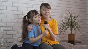 Children with a microphone. Cheerful sisters sing into the microphone together.