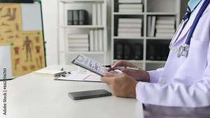 Doctor reading patient history and documenting medical records in office at hospital. Doctor writing a prescription on the desk.