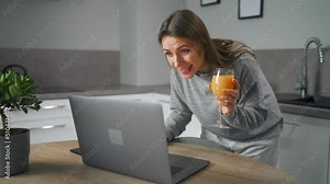 Woman standing in home cozy kitchen, leaning over the table and communicates via video link with family or close friends