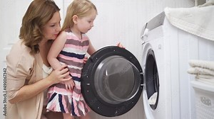 mother and daughter open the washing machine and take out the laundry