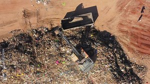 Scrapyard work - Excavator loading piles of scrap metal onto a parked trailer, Aerial view.