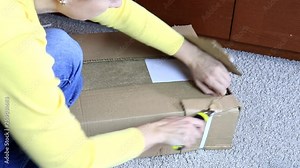 Woman unboxing a cardboard box with new furniture with construction or office knife - moving to new house and purchasing new furniture