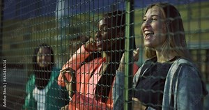 Group of Young Excited Multiracial Female Fans Cheering for Their Friends' Team Victory on Basketball Outdoor Court During Friendly Game Match. Girls Smiling and Clapping While Watching Through Fence