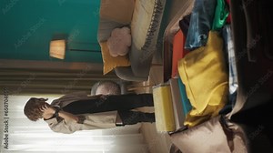 Vertical video of a teenager, teen, young man having a call on the background while packing a suitcase laying on the foreground, poitning at it, discussing something.