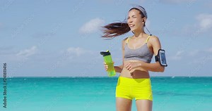 Tired female runner sweating after cardio exercise. Asian running woman sweating post workout swiping head exhausted or touching forehead drinking water from bottle. Exhaustion / dehydration concept.