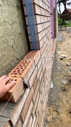 Laying hollow bricks with mortar and aligning rows to build exterior house wall