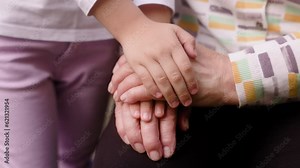 A little girl places her hand on her grandmother's hand, and the grandmother places her hand on the granddaughter's hand. A combination of generations. Family, closeness, support, and help.