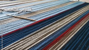 Multicolor wool threads in closeup on a weaving board with weaving needle, pan left