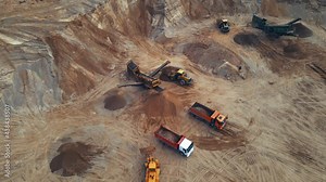 Front end loader loading sand into dump truck in open pit. Jaw crusher sand making production line. Heavy mining machinery working in quarry. Truck transports minerals from opencast.