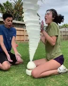 Two friends wrap rubber bands around milk jug until it explodes all over one of them.
