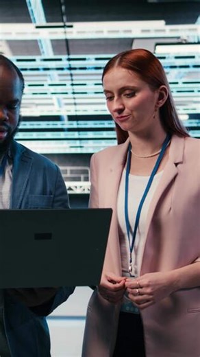 Vertical Engineering team in server hub working together with laptop to do maintenance tasks on machines. Teamworking colleagues in modern high tech data center configuring server settings, camera A