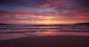 Sea waves splashing on the beach sand at sunset, tropical ocean shore during scenic sunrise with clouds