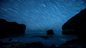 Star trails above the rocky seashore. Time lapse.