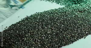 A hand with a one hundred bill stirs chia seeds in green light. This video can be used as a display of the chia crypto coin. High quality 4K footage