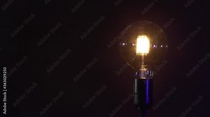 Incandescent light bulb isolated on black background. Glass and metal base. Lights up brightly with blinking and fades out. Edison lamp. 4K resolution
