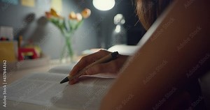 Closeup young Asia teen girl student distance learning lesson and doing homework sitting at desk in living room at house night. Work from home, Social distance, quarantine for corona virus prevention.