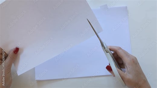 Pair of scissors is cutting a piece of paper. The paper is white and has a red border