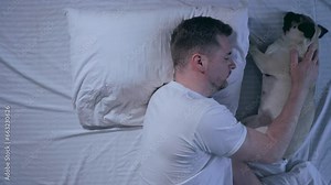 The dog sleeps next to the owner on the bed. A man hugs his dog in a dream.