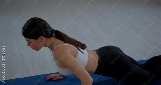 Young woman performs prone abdominal stretch in fitness studio during morning workout session