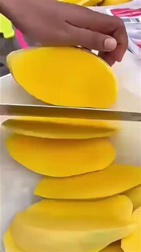 A mango that is being split using a sharp knife by a chef
