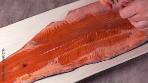 Deboning raw trout fillet. Taking out fish bones with tweezers. Preparing to cook seafood meal