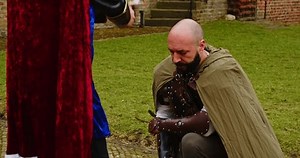 A fantasy knight kneeling for the King and being knighted with a plastic sword
