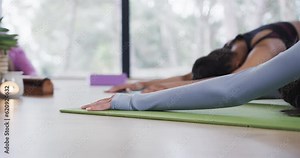 Diverse women with arms raised practicing child pose around plant, candle, singing bowl