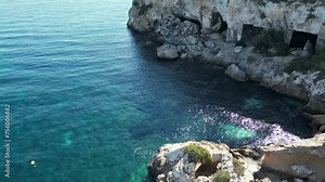 Vista aérea estática de las cuevas de la playa del mago en Mallorca. Agua transparente, yates e embarcaciones fondeados. Dia de sol en verano.