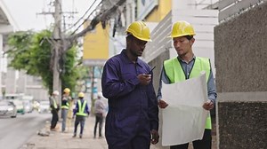 Structural engineers and construction workers are holding blueprints inspecting structure. sky train track construction in city. Blue collar wears a safety hardhat while working on construction site.
