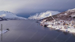 Snow covered mountain range on coastline in winter, Norway. Surroundings of town Tromso. Panoramic aerial view landscape of nordic snow cowered mountains, houses and ocean. Troms county, Fjordgard
