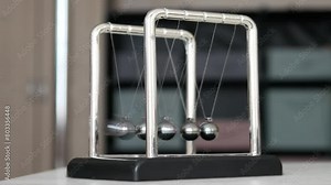 A Newton's cradle on the table close-up and a child's fingers pulling back one sphere and releasing it starting the pendulum