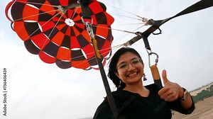 4K shot of adventurous girl doing parasailing and giving thumbs up at Jaisalmer, Rajasthan, India. Girl on vacation doing adventure activity.
