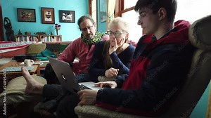 Family points and talks to a laptop computer screen in a living room setting.