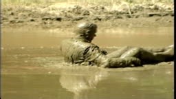 Man in Suit and Tie Swimming and Splashing Around in Mud Pit