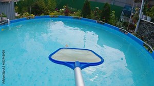 Net-skimmer removes leaves from the surface of the backyard pool water. Servicing and caring for your home pool with a netting skimmer. The camera is mounted on the handle of the skimmer