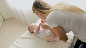 Beautiful young mother undressing her 3 months old baby boy lying on changing table