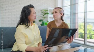 Asian elderly mother worried about health check results after looking at the x-ray screening film. Caring daughter and mother checking xray screening films of bones for checkup. Health care concept