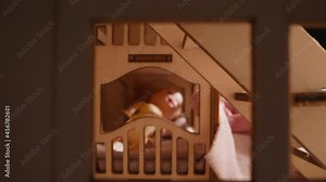 Little child hand carries soft fabric sheet to cover dolly lying in bed in large toy house close zoom in though room with steps and window