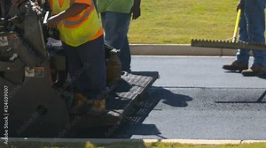 Close Up Road Workers Smooth Asphalt in Slow Motion. road workers flatten and smooth asphalt on a newly paved road in slow motion