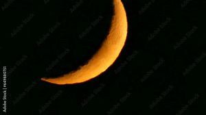 Dark night sky and orange and yellow crescent moon with visible fragments of craters - natural view before moonset in real time. Topics: astronomy, optical phenomenon, atmosphere, cosmos, science