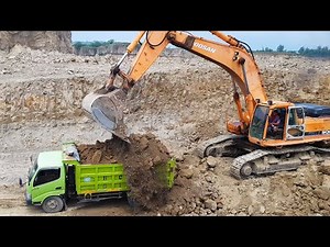 Trucks work alongside doosan excavator digging sand and rock on extreme hills