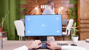 POV shot of man typing on computer with green screen in a modern workplace.