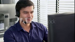Young competent asian male call center agent working at his computer while simultaneously speaking with customers. Concept of an operator, customer service agent working in the office with headset.